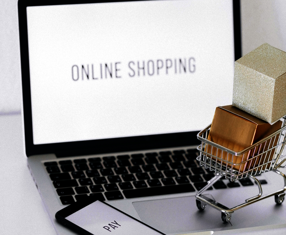 Online shopping. Image of a laptop with a cell phone next to it along with a mini shopping cart with packages in it.